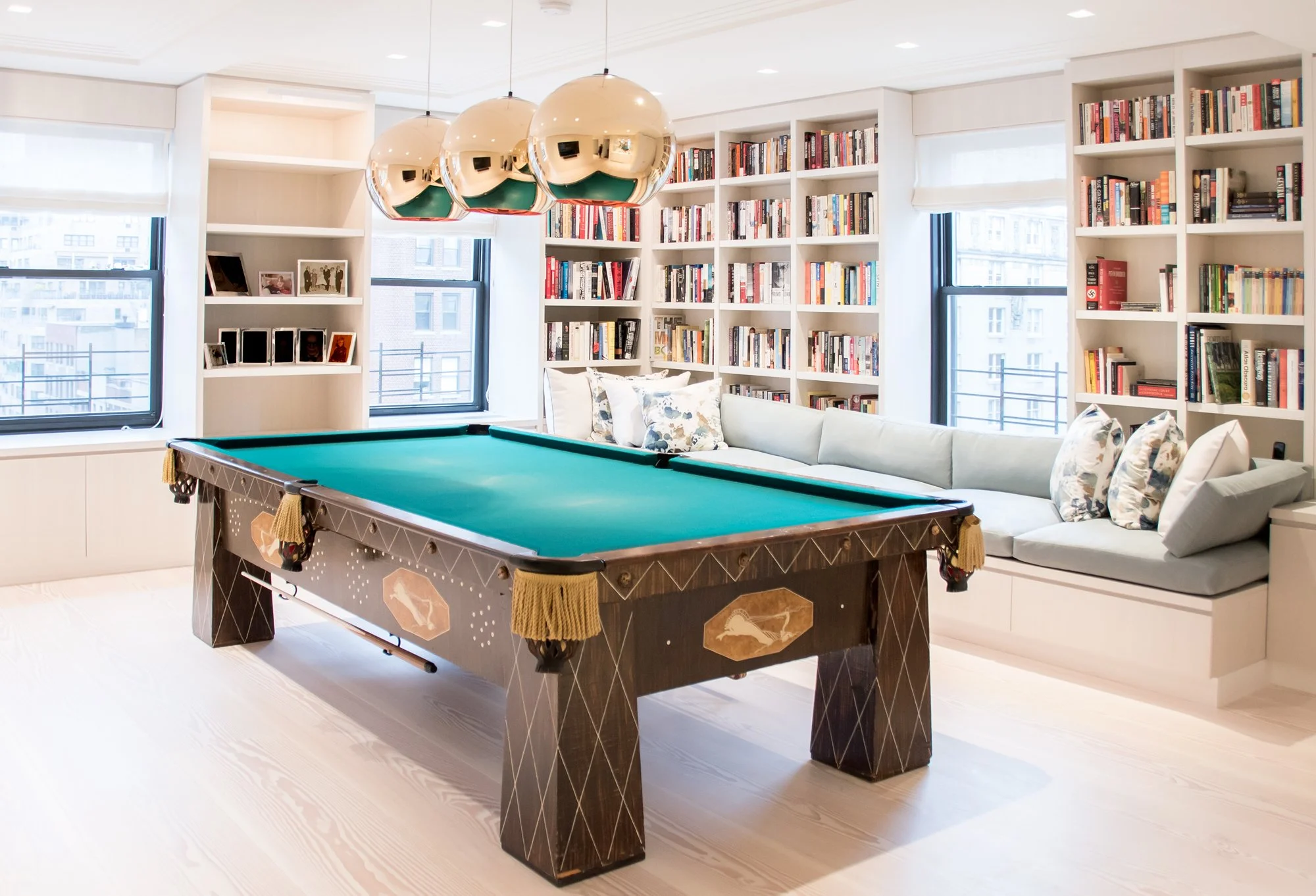 Bespoke architectural millwork for a luxury library featuring white cabinetry, integrated window seating, and modern metallic pendant lighting.