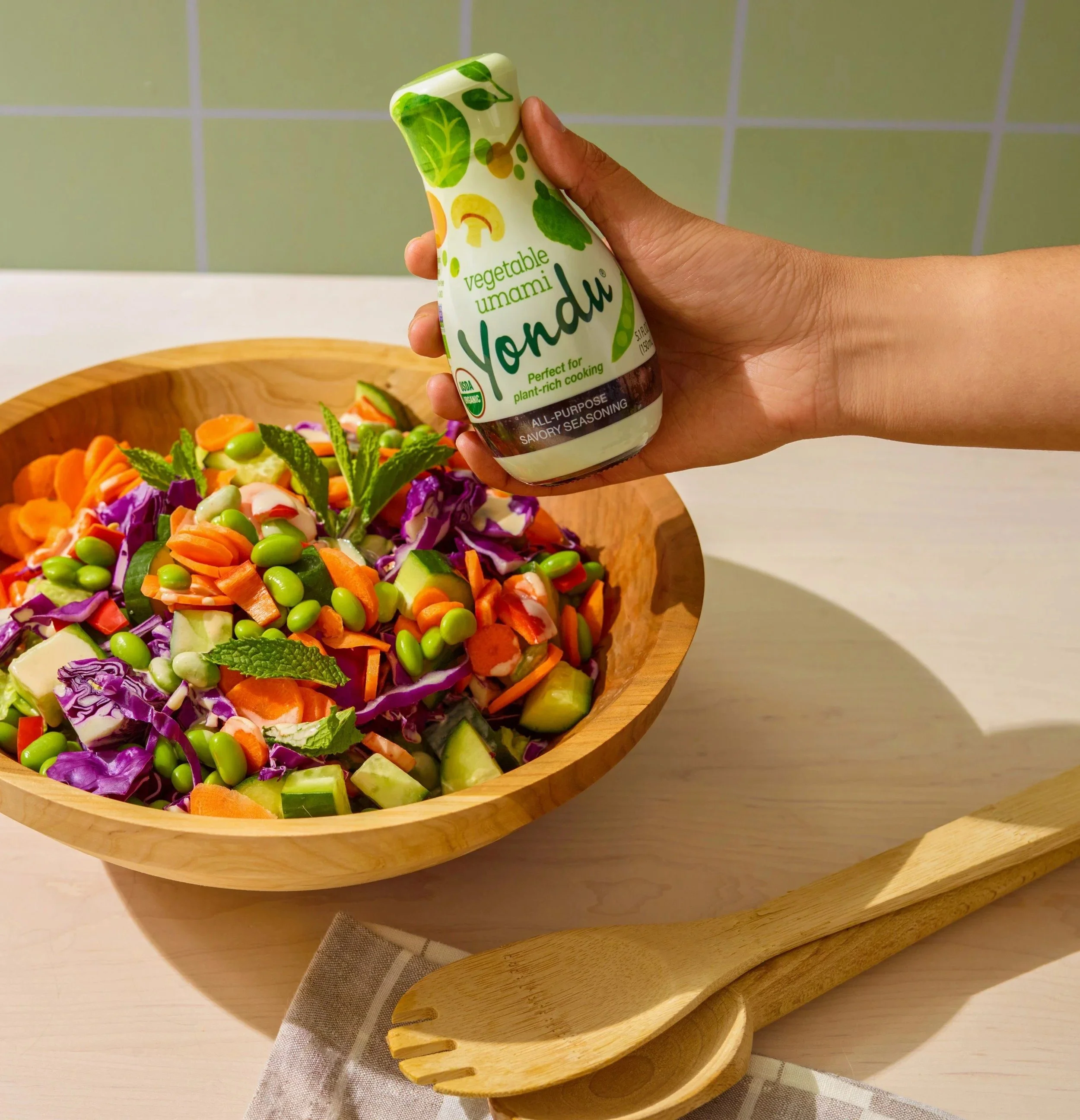 Hand drizzling umami sauce over a colorful salad bowl, CPG food photography