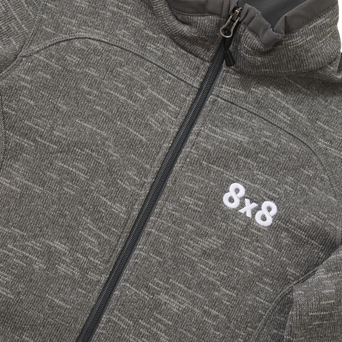 Close-up of a gray zip-up jacket with a patterned texture and the text '&x8' embroidered in white.