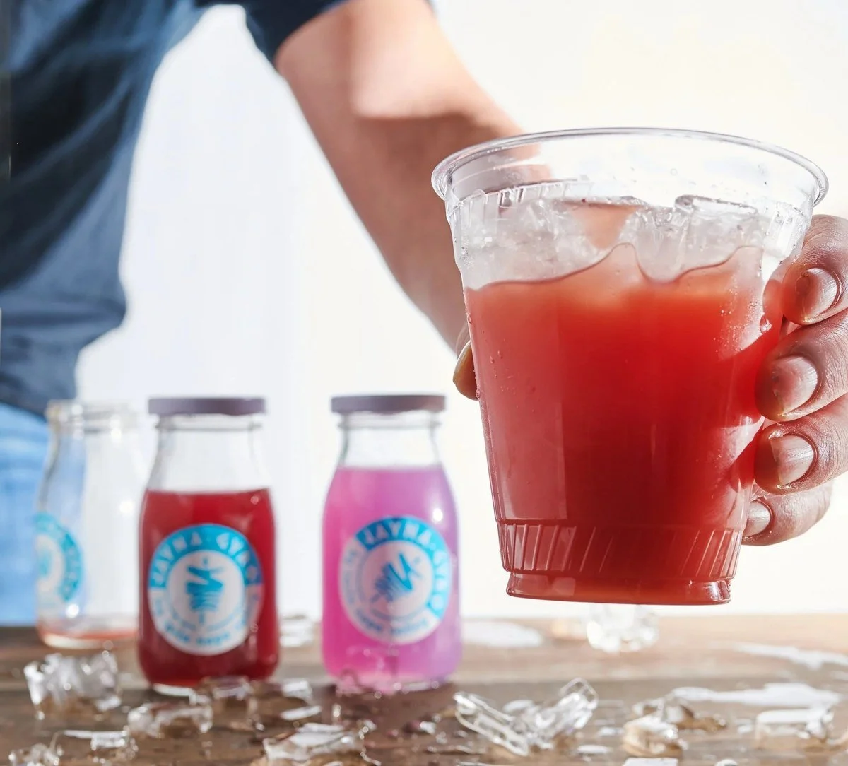 Hand holding an iced red drink with bottled drinks