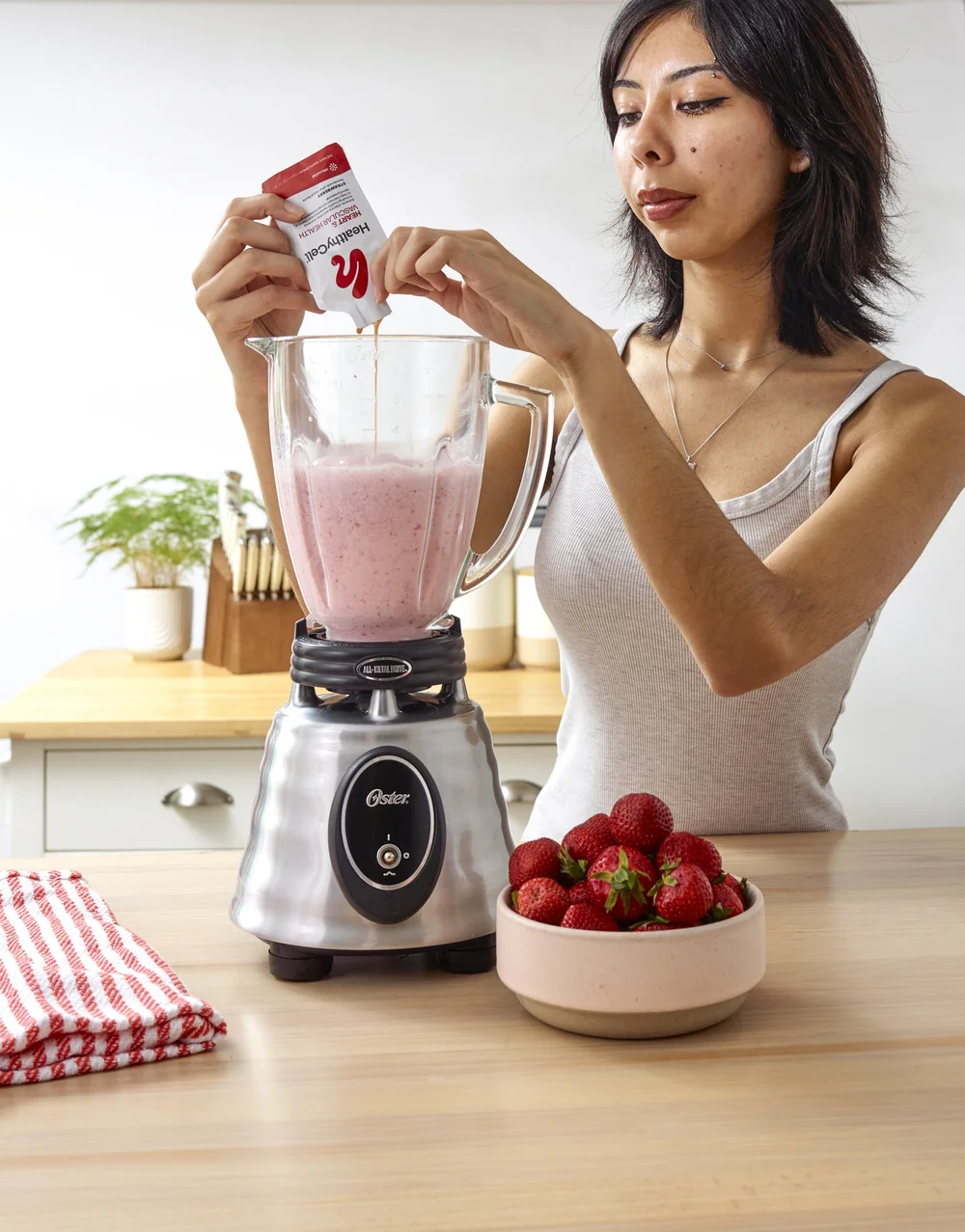 Woman adding a strawberry supplement to a smoothie, supplement lifestyle photography