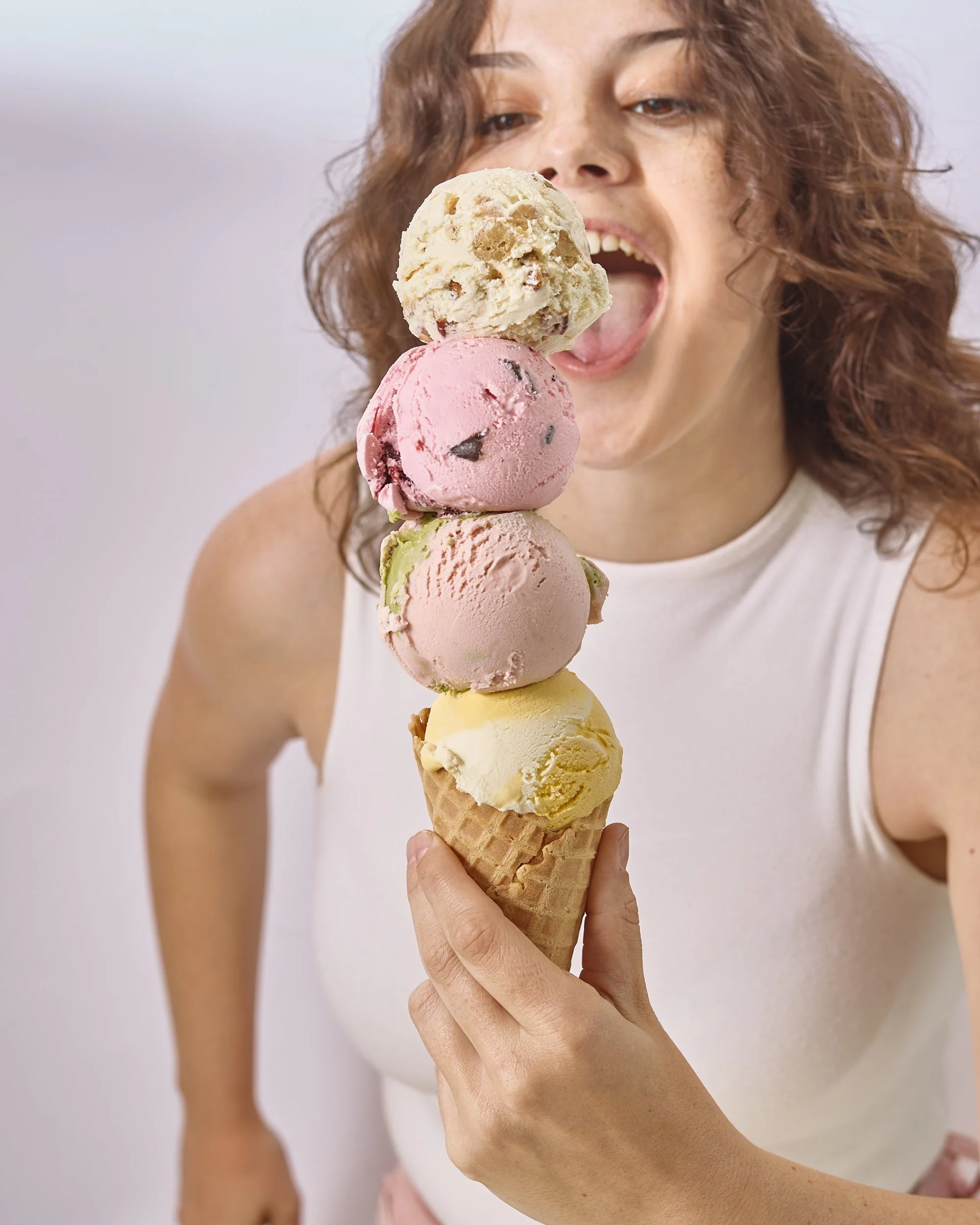 Woman holding a waffle cone with four scoops of colorful ice cream.