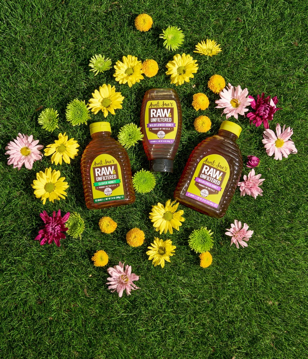 Honey bottles on grass surrounded by fresh flowers