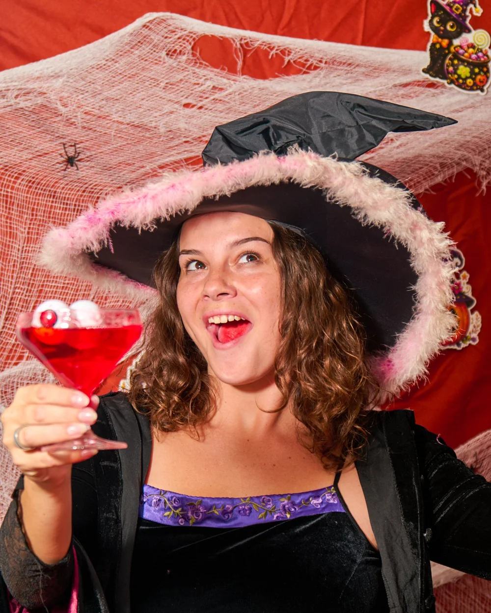 Witch with a glass of blood red punch on a Halloween set