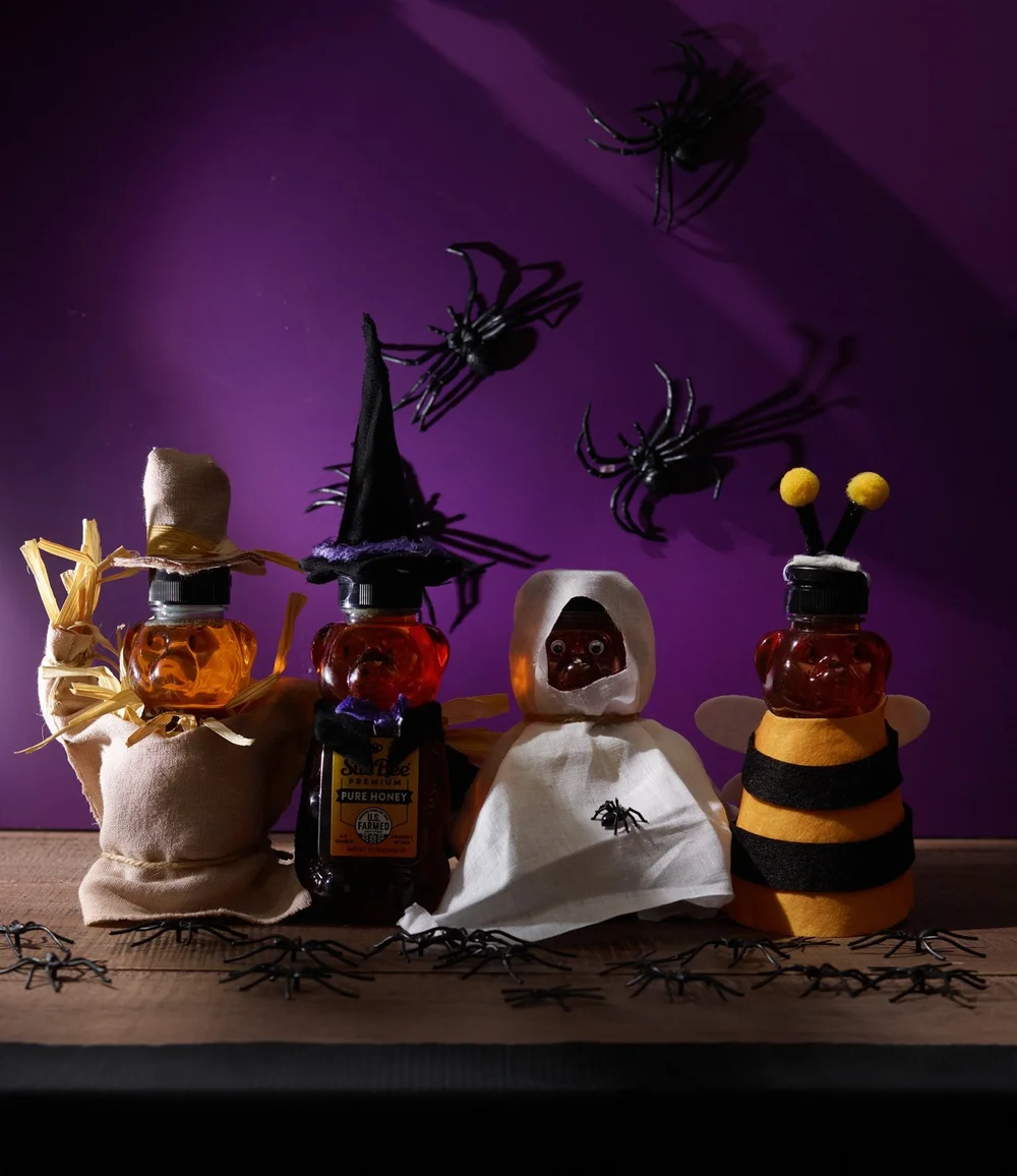 Honey bottles dressed in Halloween costumes on a purple set