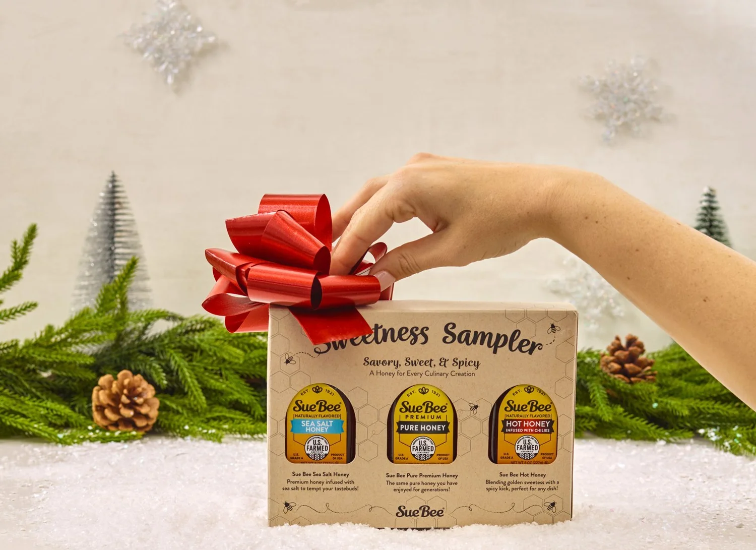 Hand adding a red bow to a holiday gift sampler