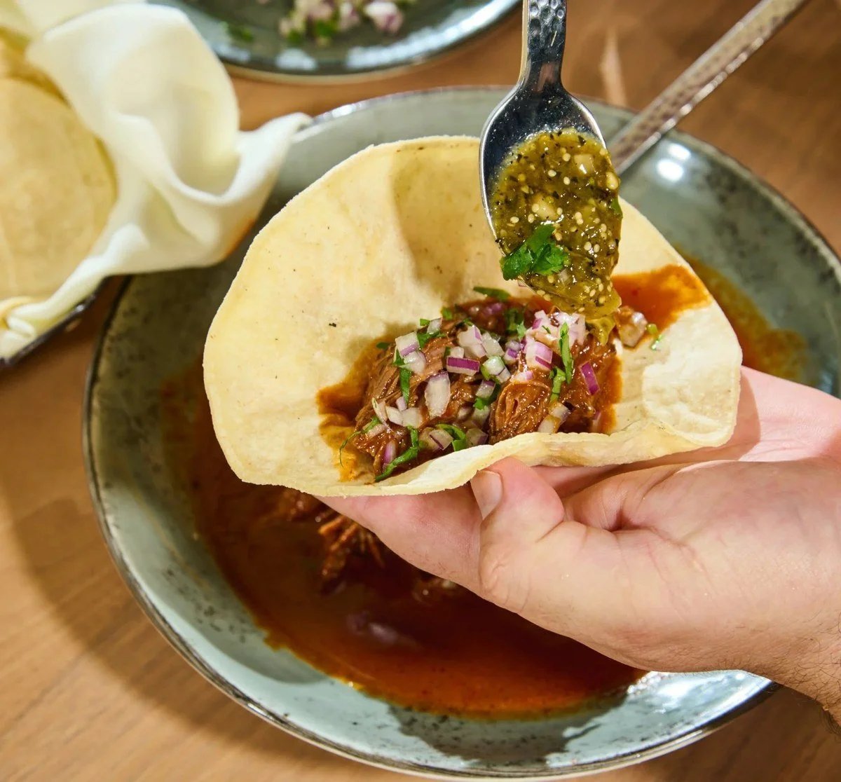 Green salsa being spooned onto a taco
