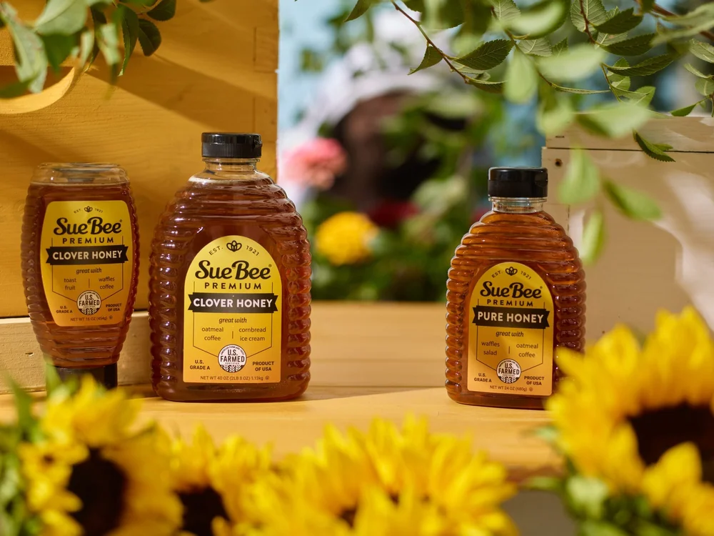 Sue Bee Premium honey bottles in sunlight with sunflowers and beehive boxes, CPG photography