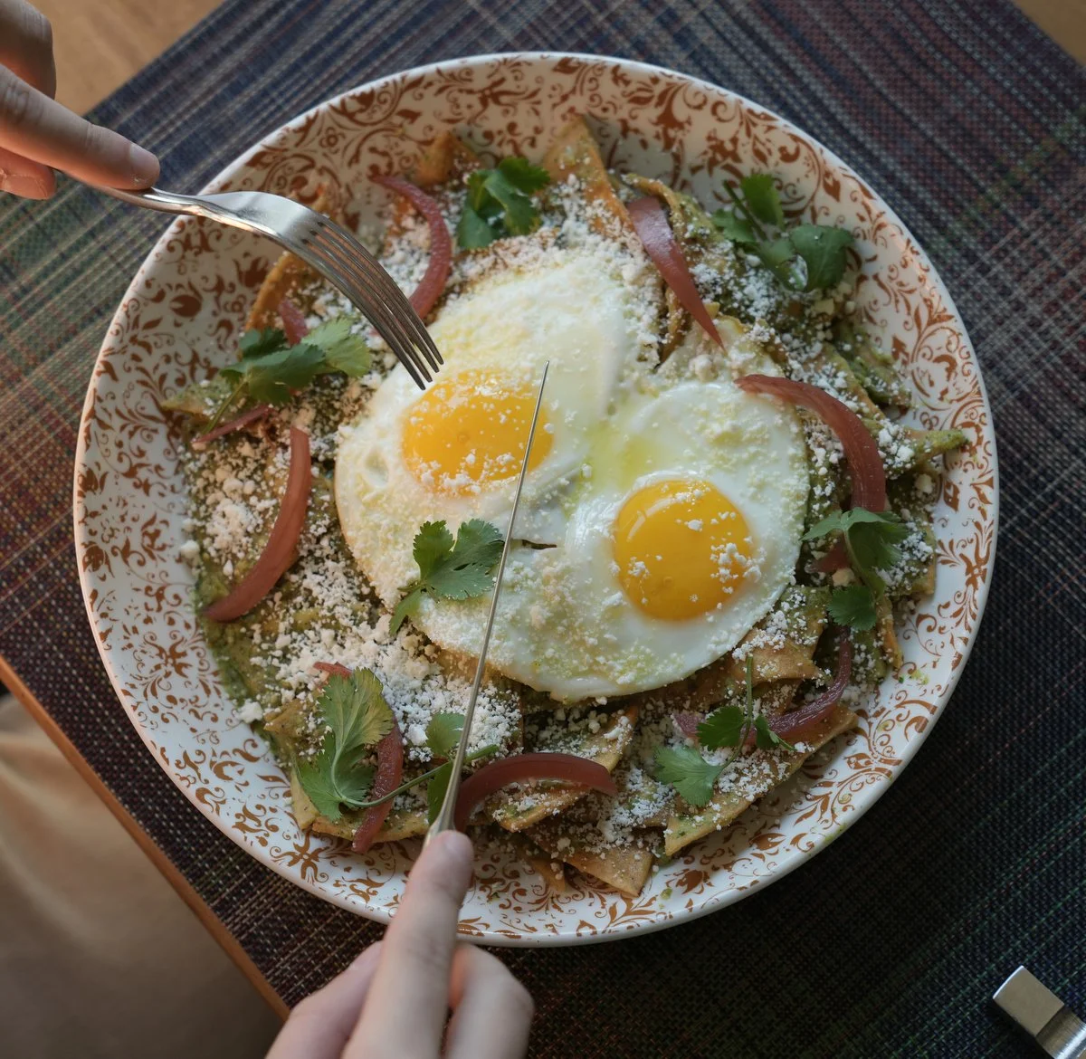 Overhead plate of fried eggs and greens being cut