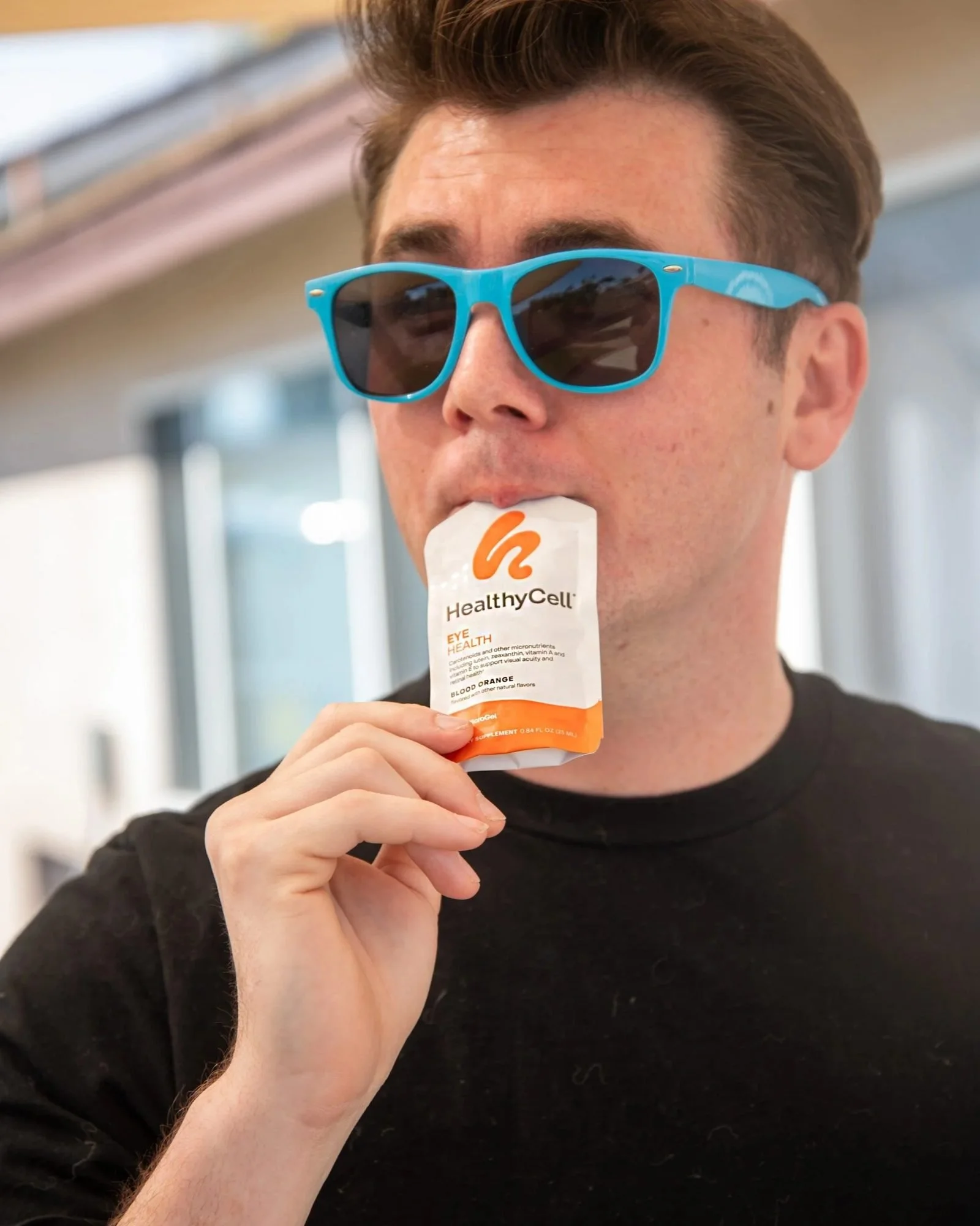 Man in blue sunglasses sipping a Healthy Cell supplement pouch, CPG lifestyle photography