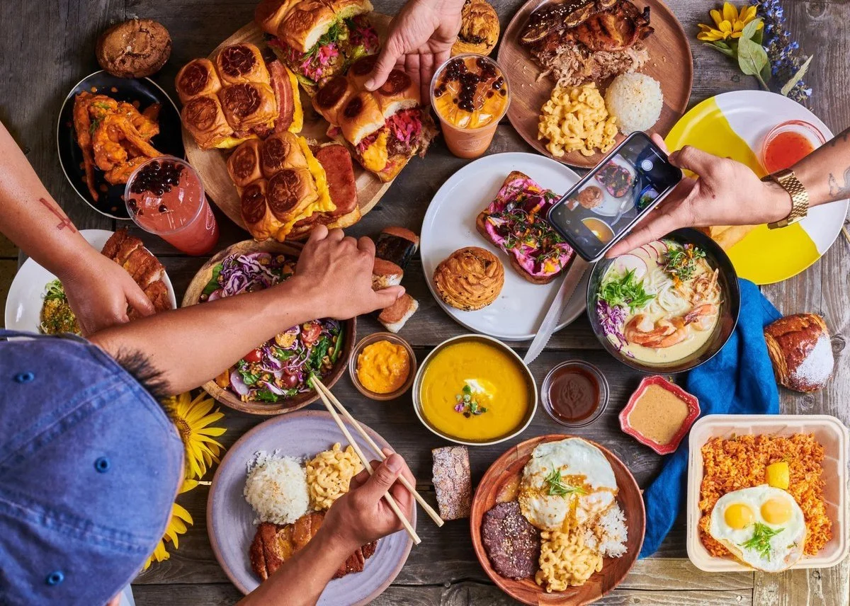 Overhead view of a shared table spread with hands reaching for dishes