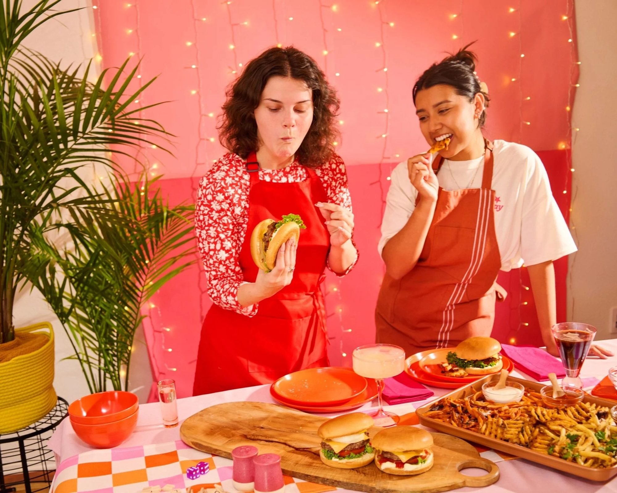 Two women tasting burgers at a pink party table, food lifestyle photography