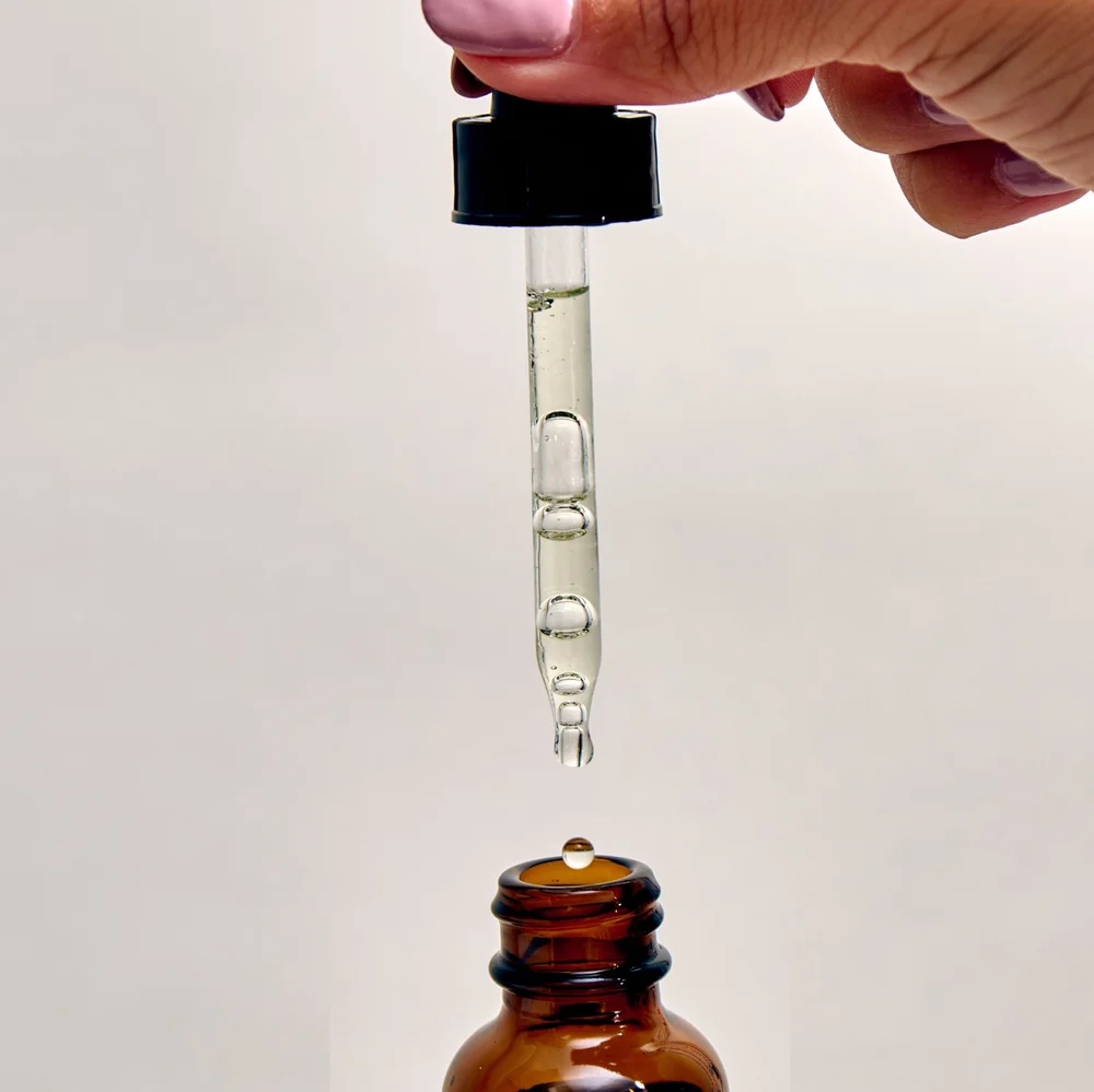A dropper above a small brown glass bottle with a drop of liquid about to fall into it.