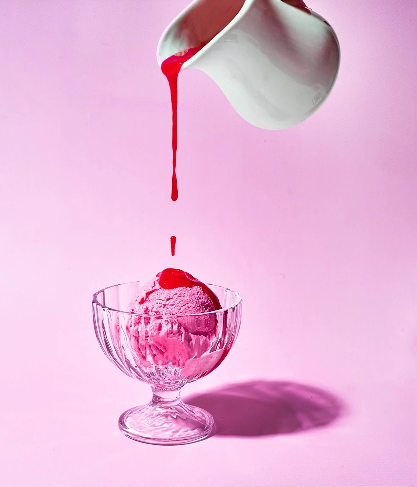 Food styling: raspberry sauce poured over ice cream in a glass dish