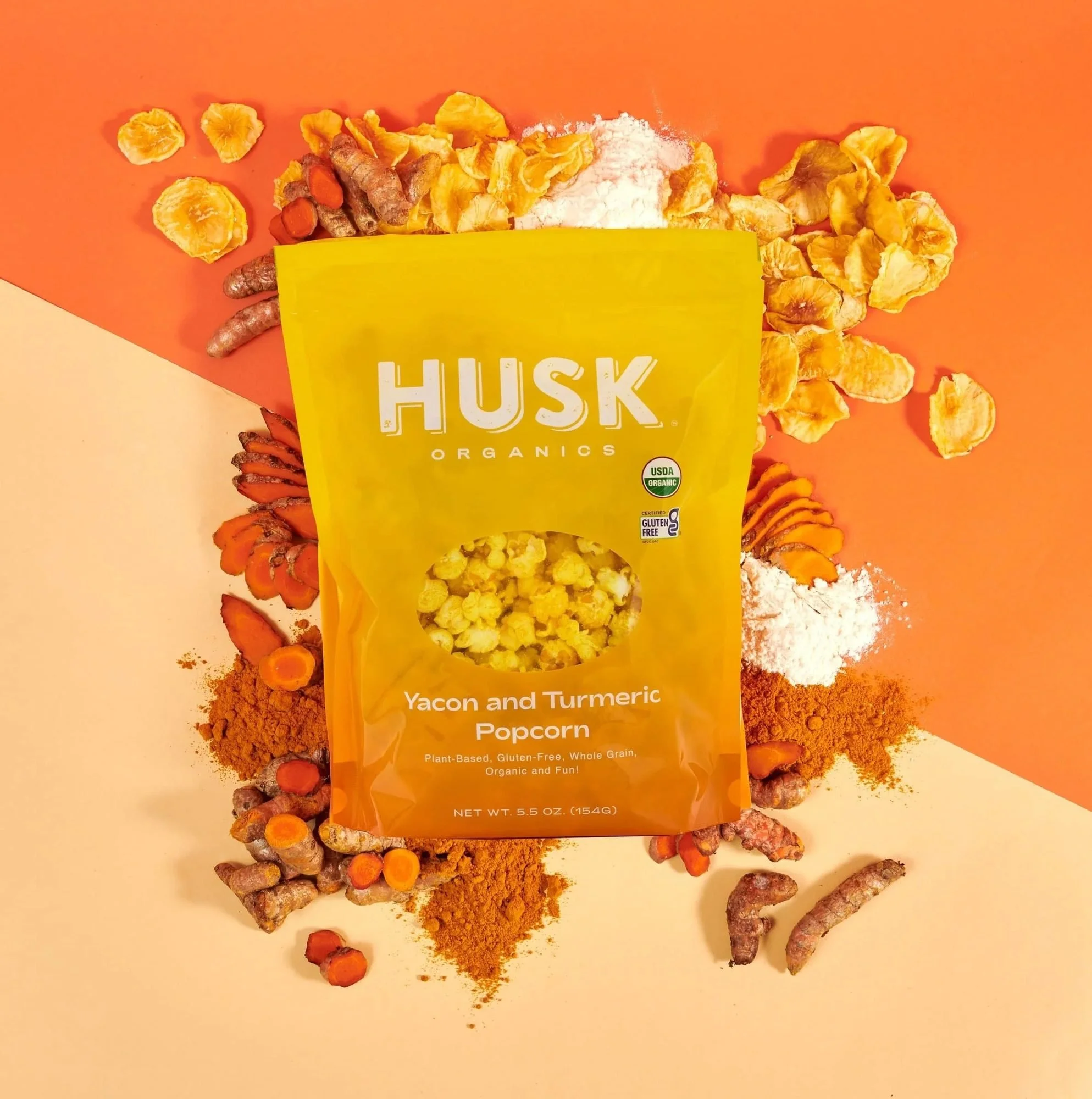 Husk Organics turmeric popcorn bag with spices on orange, CPG snack photography