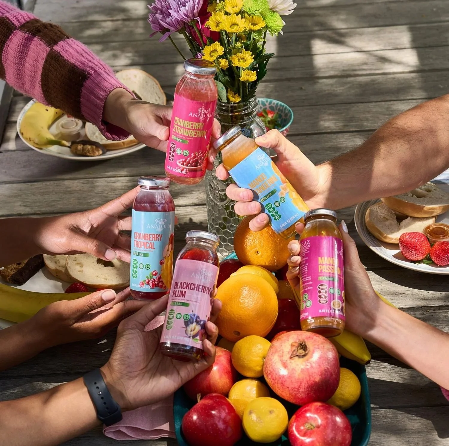 Friends toasting bottled drinks over a fruit-filled table, CPG beverage lifestyle photography