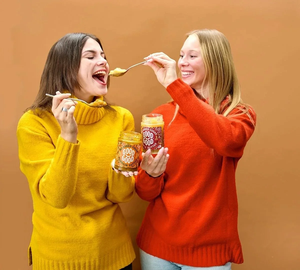 Two friends in yellow and red sweaters tasting Good Good jam on orange, color-blocked CPG lifestyle photography