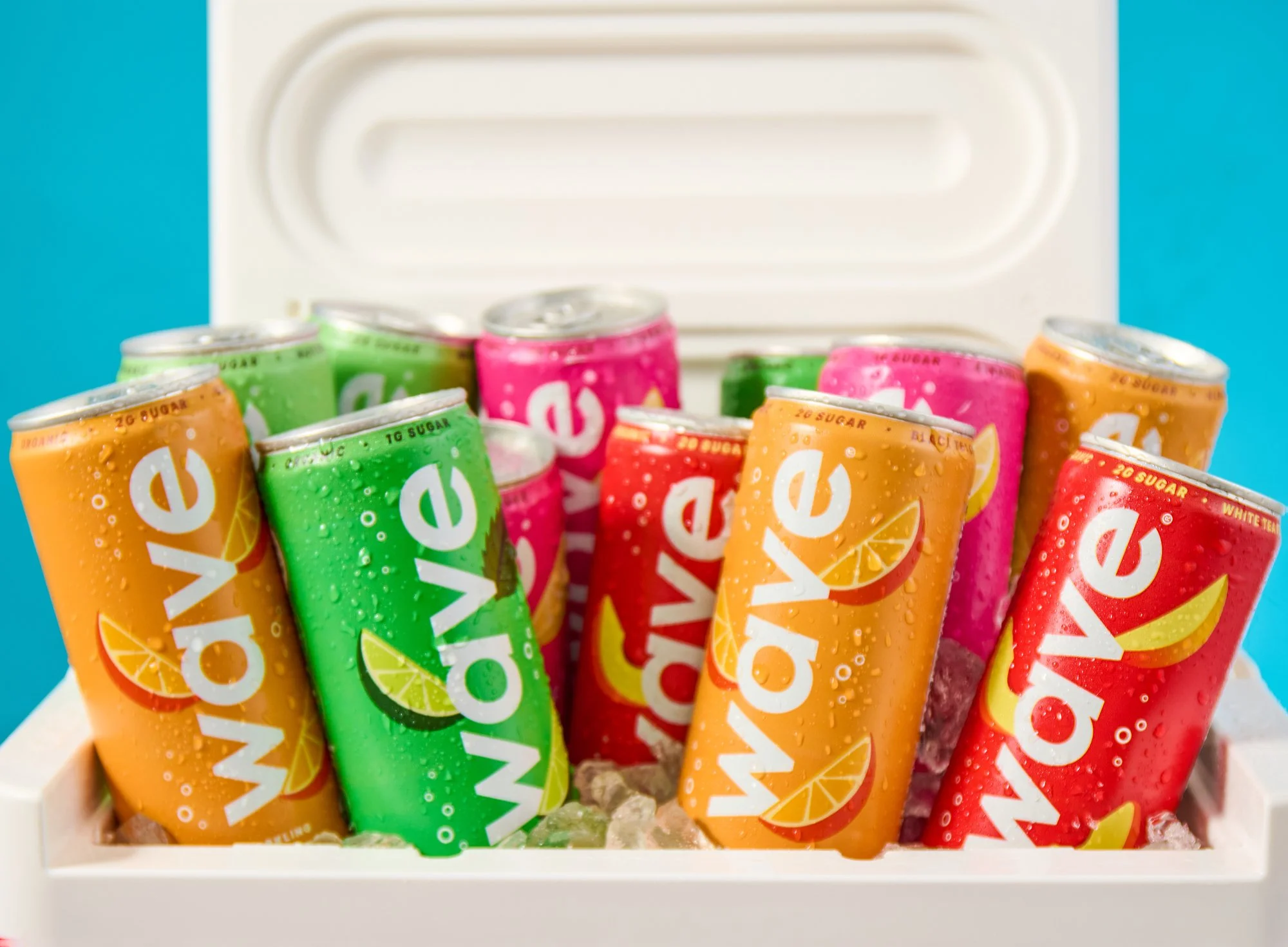 A collection of colorful cans of Wave soda in various flavors, placed in a white cooler with ice, against a blue background.