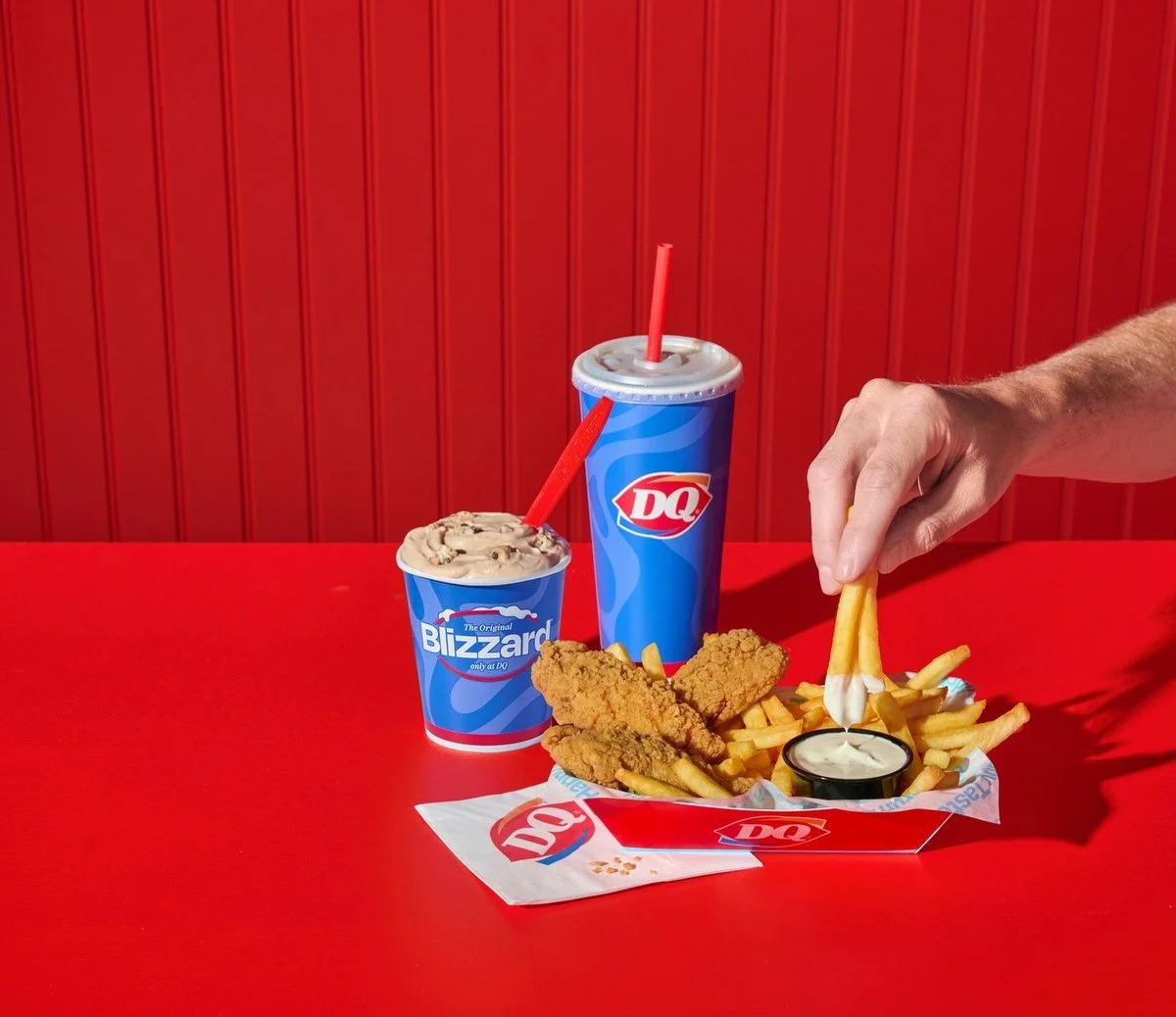 Hand dipping Dairy Queen fries on a red background