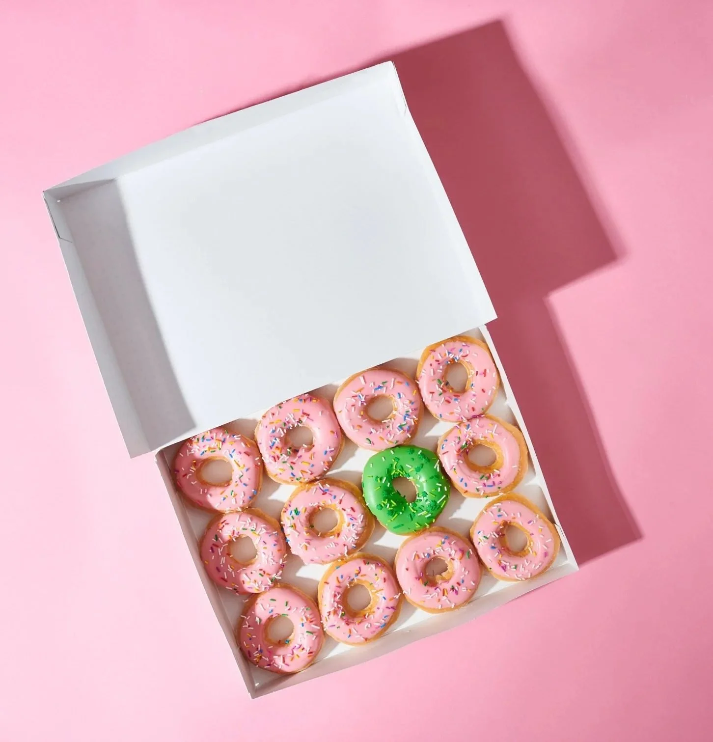 Open bakery box of pink frosted donuts on a pink background. Clean, colorful product and dessert photography.