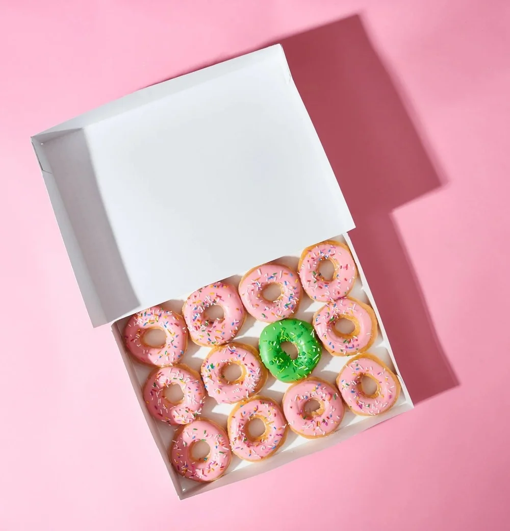 Open bakery box of pink frosted donuts on a pink background. Clean, colorful product and dessert photography.