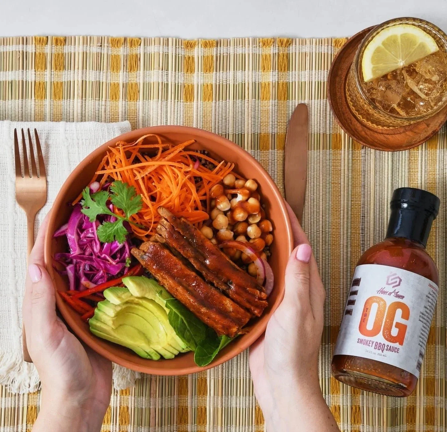 Hands holding a grain bowl next to Hero of Sauce The OG BBQ sauce, CPG food photography