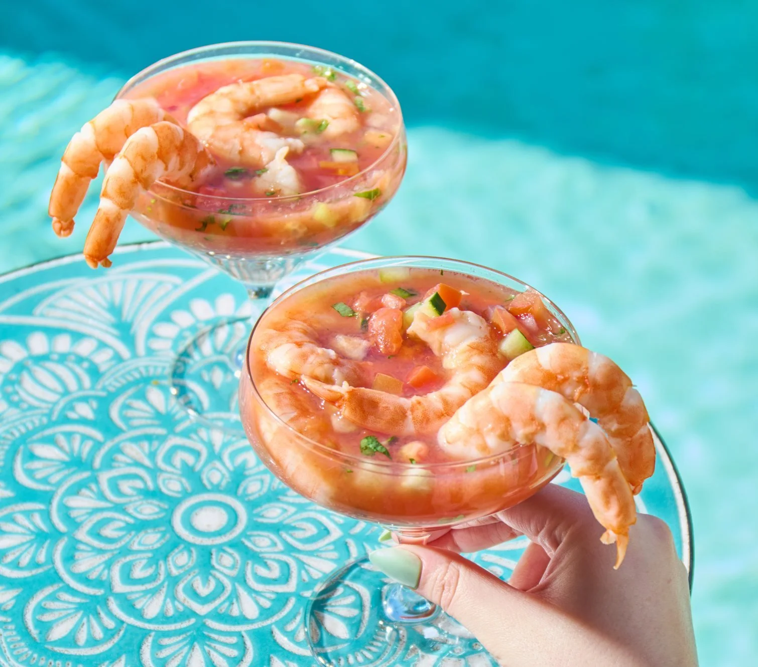 Shrimp cocktails in glasses on blue tile by a pool. Summer lifestyle food photography for grocery brands.