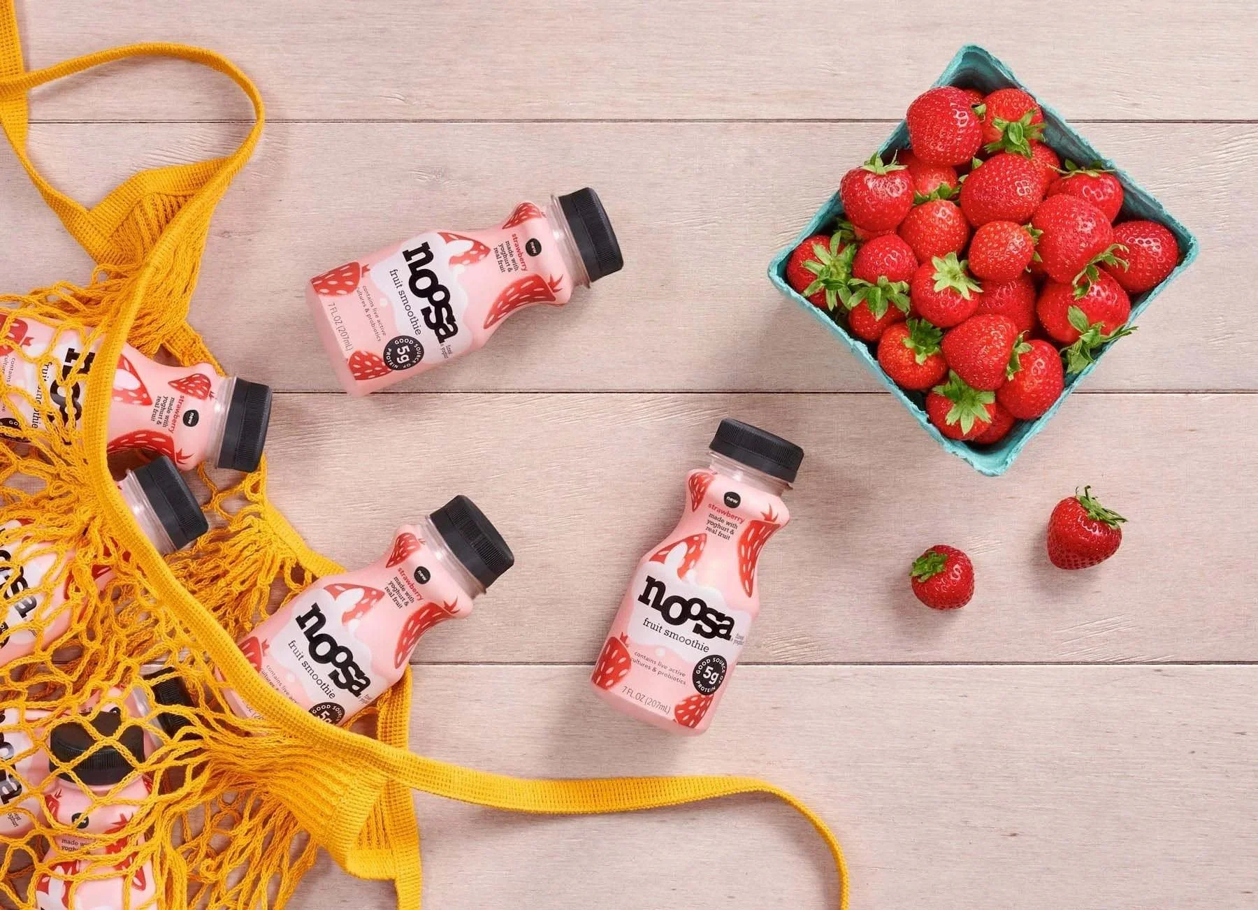 Noosa strawberry drinks in a mesh bag with fresh strawberries, CPG lifestyle photography