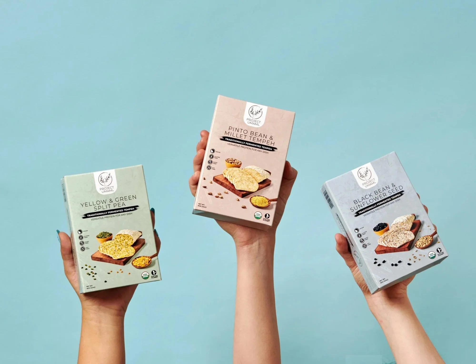 Three hands holding snack boxes up on blue, CPG lifestyle photography