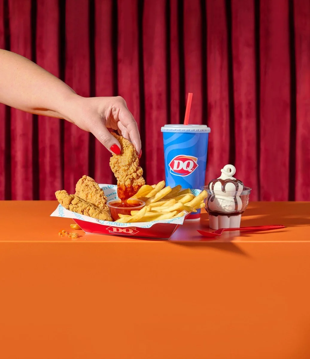 Hand dipping a Dairy Queen chicken strip in front of a red curtain