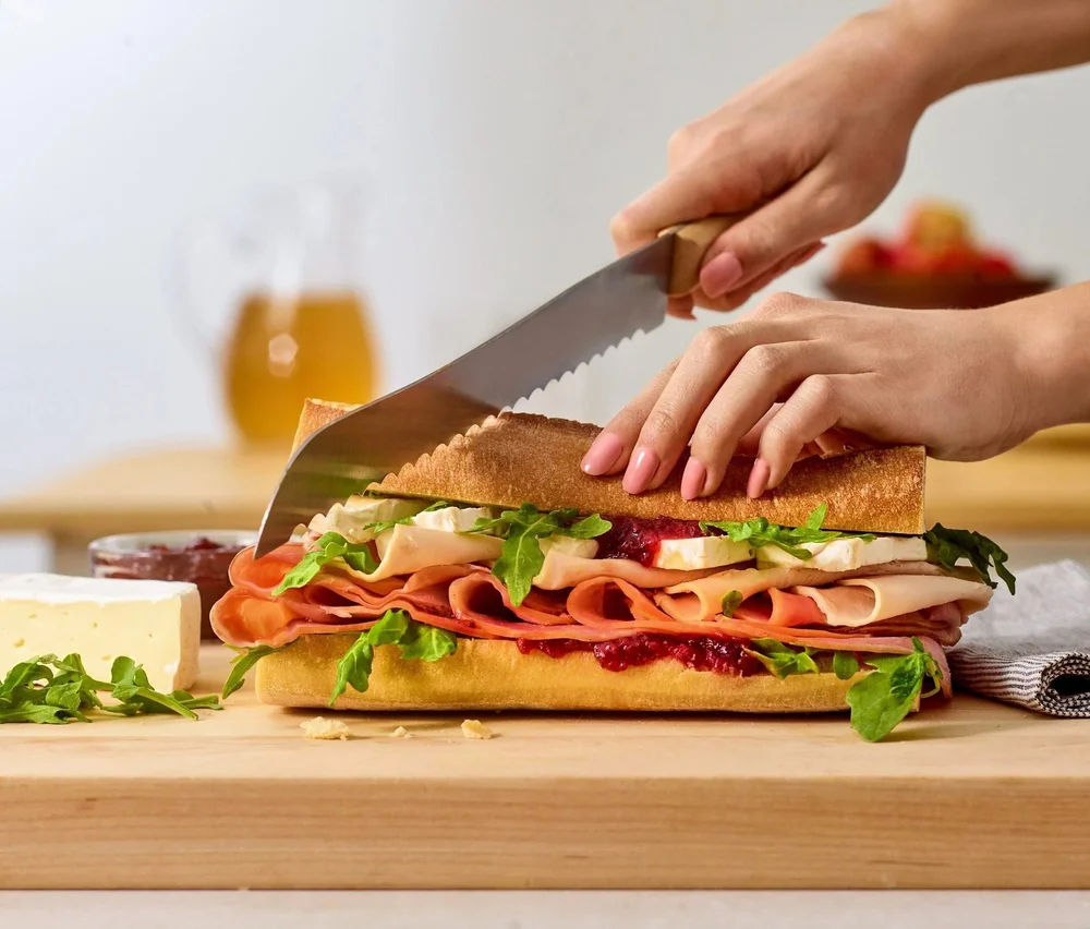 Knife slicing a loaded sub sandwich on a board. Deli and sandwich food photography with action.