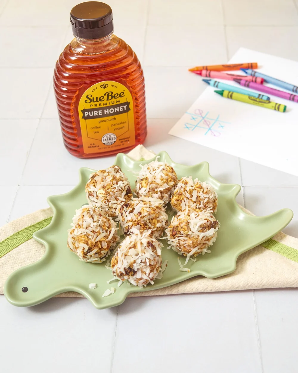 Sue Bee honey coconut energy balls on a green plate with a honey bottle. Kid-friendly recipe photography for a honey brand.