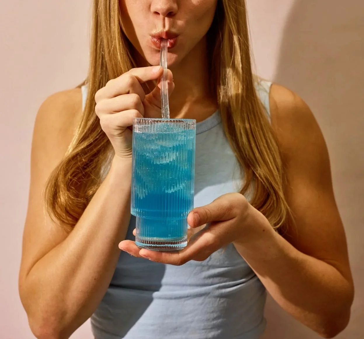 Woman sipping a blue drink through a glass straw, beverage lifestyle photography