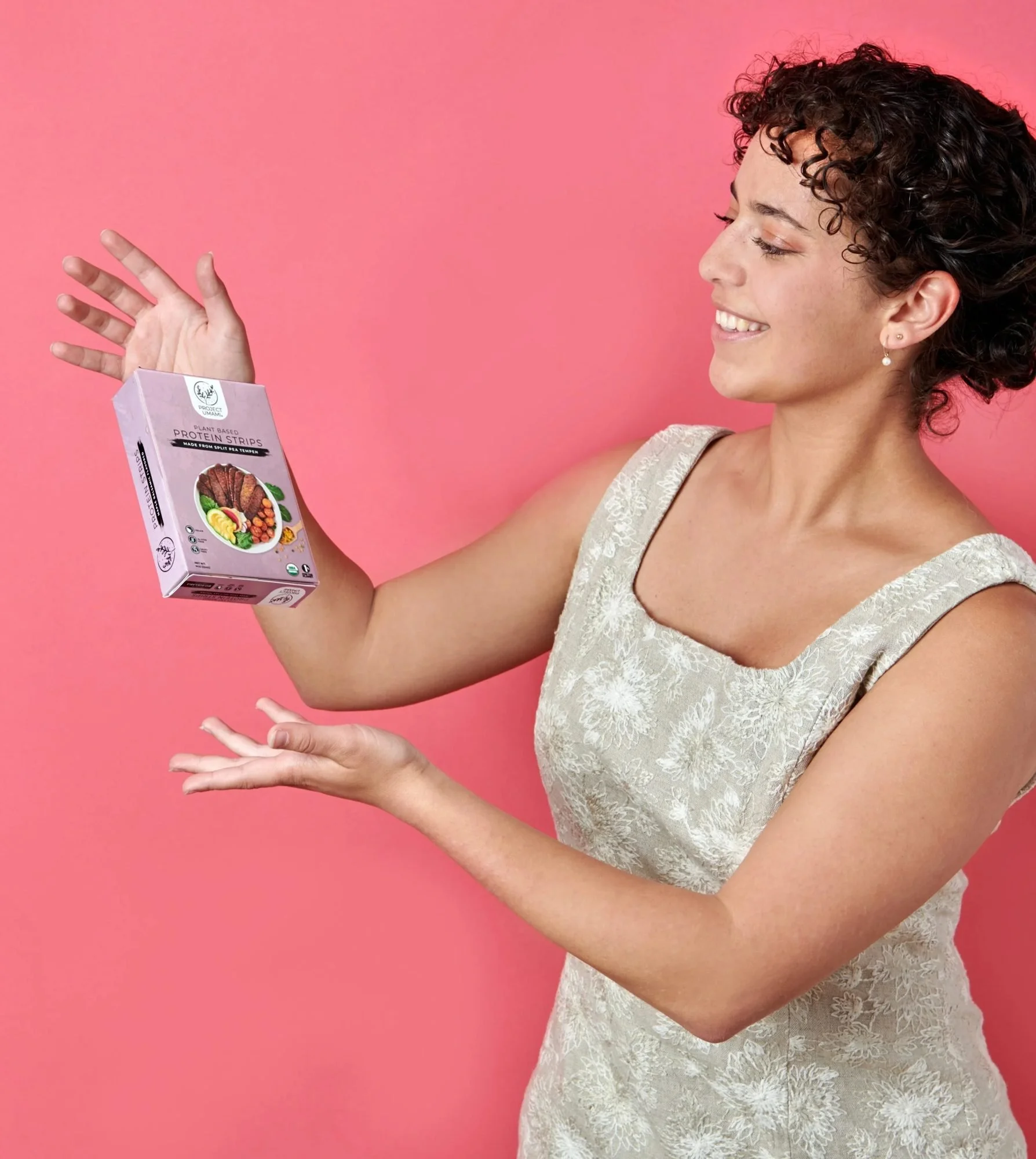 Model tossing a snack pouch on pink, CPG lifestyle photography