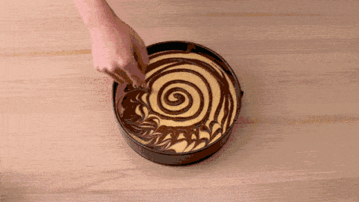 Stop motion GIF of pumpkin swirl marbling into cheesecake. Animated dessert recipe content.