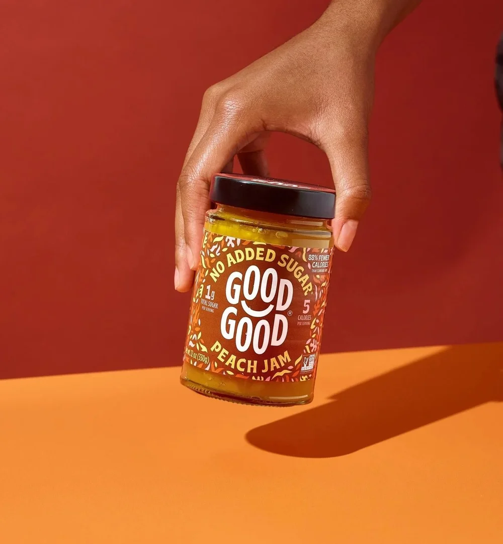 Hand placing a Good Good peach jam jar on an orange color-blocked set, CPG photography