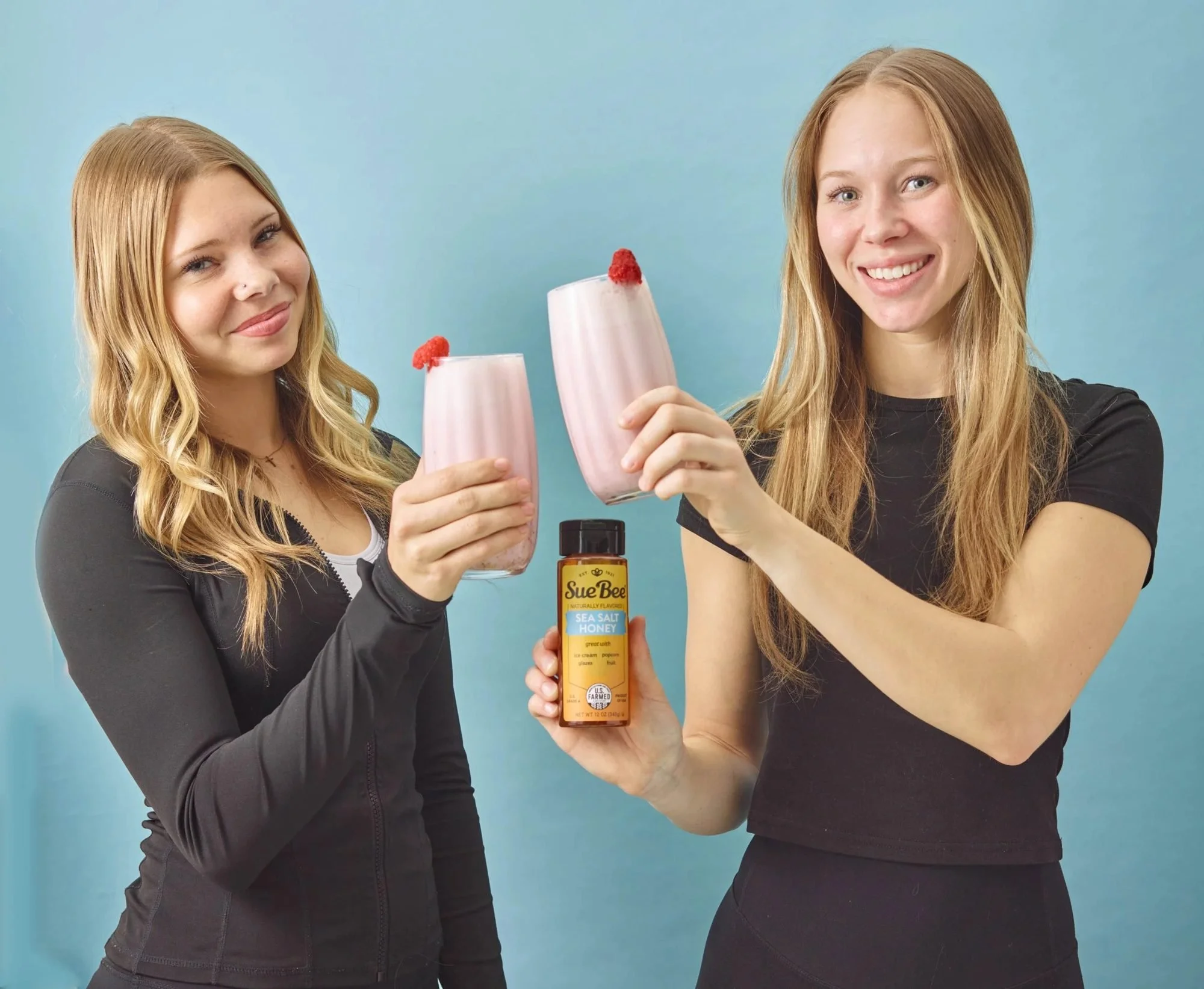 Two friends toasting pink smoothies with a honey bottle on blue, CPG lifestyle photography