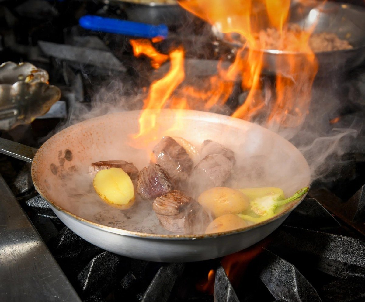 Steak and potatoes flaming in a saute pan on the restaurant line