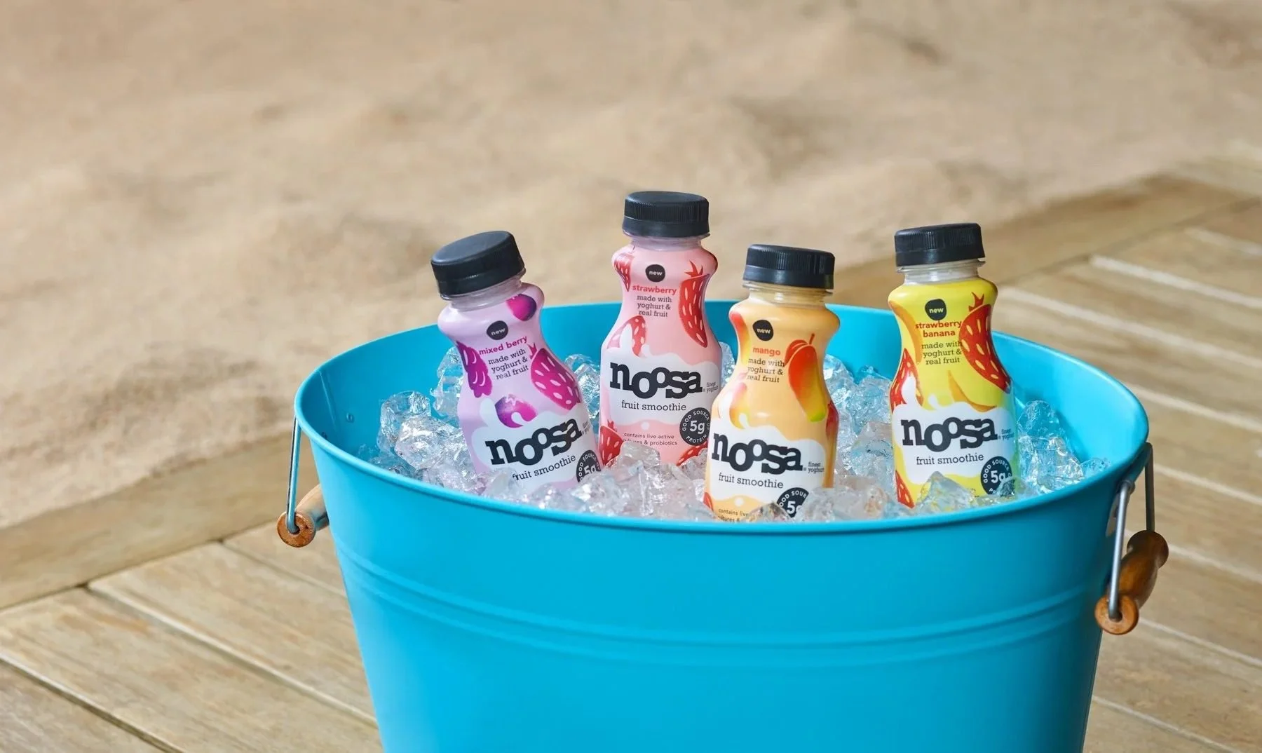 Noosa drinks in a blue ice bucket on sand, summer CPG beverage photography