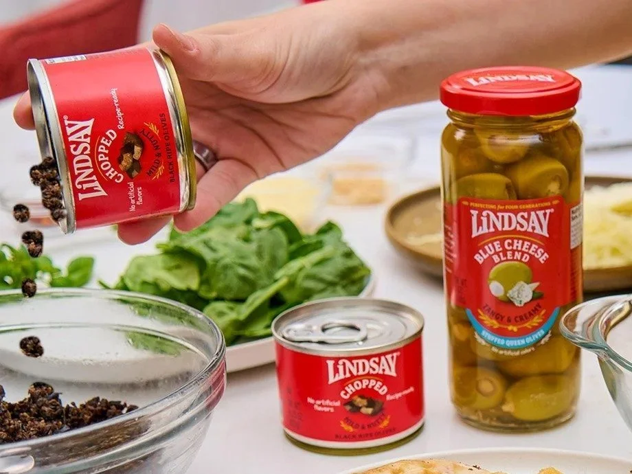 Hand pouring Lindsay chopped olives from a can next to an olive jar, CPG food photography