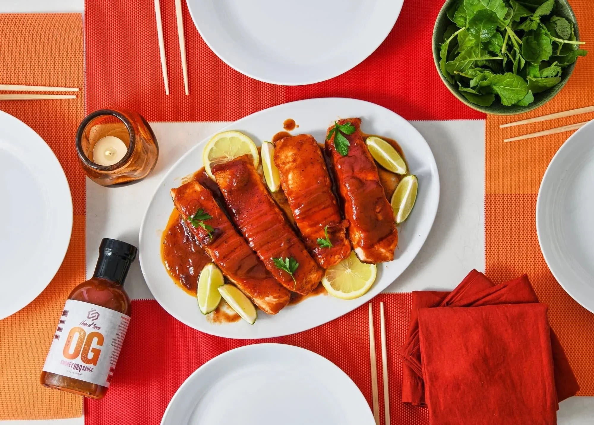 Sauced chicken with OG sauce bottle on a red table setting. CPG sauce photography in a styled tabletop scene.