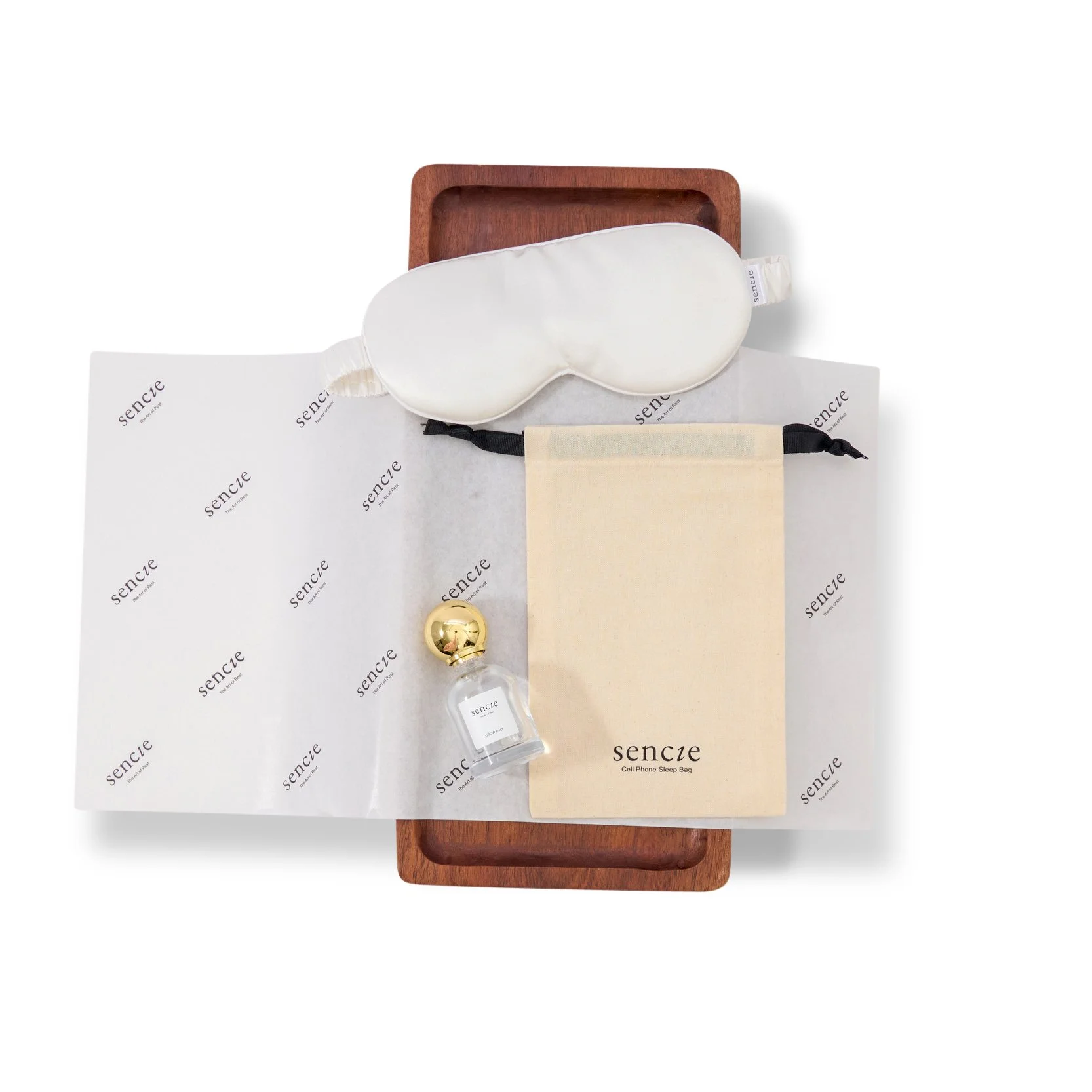 Sleep mask, small perfume bottle, and cell phone sleep bag on a wooden tray with branded paper.
