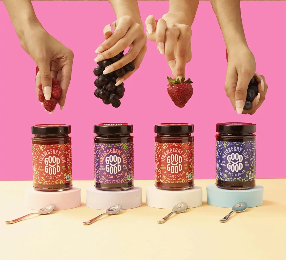 Hands placing fruit on Good Good jam jars on a pink and yellow set, CPG photography
