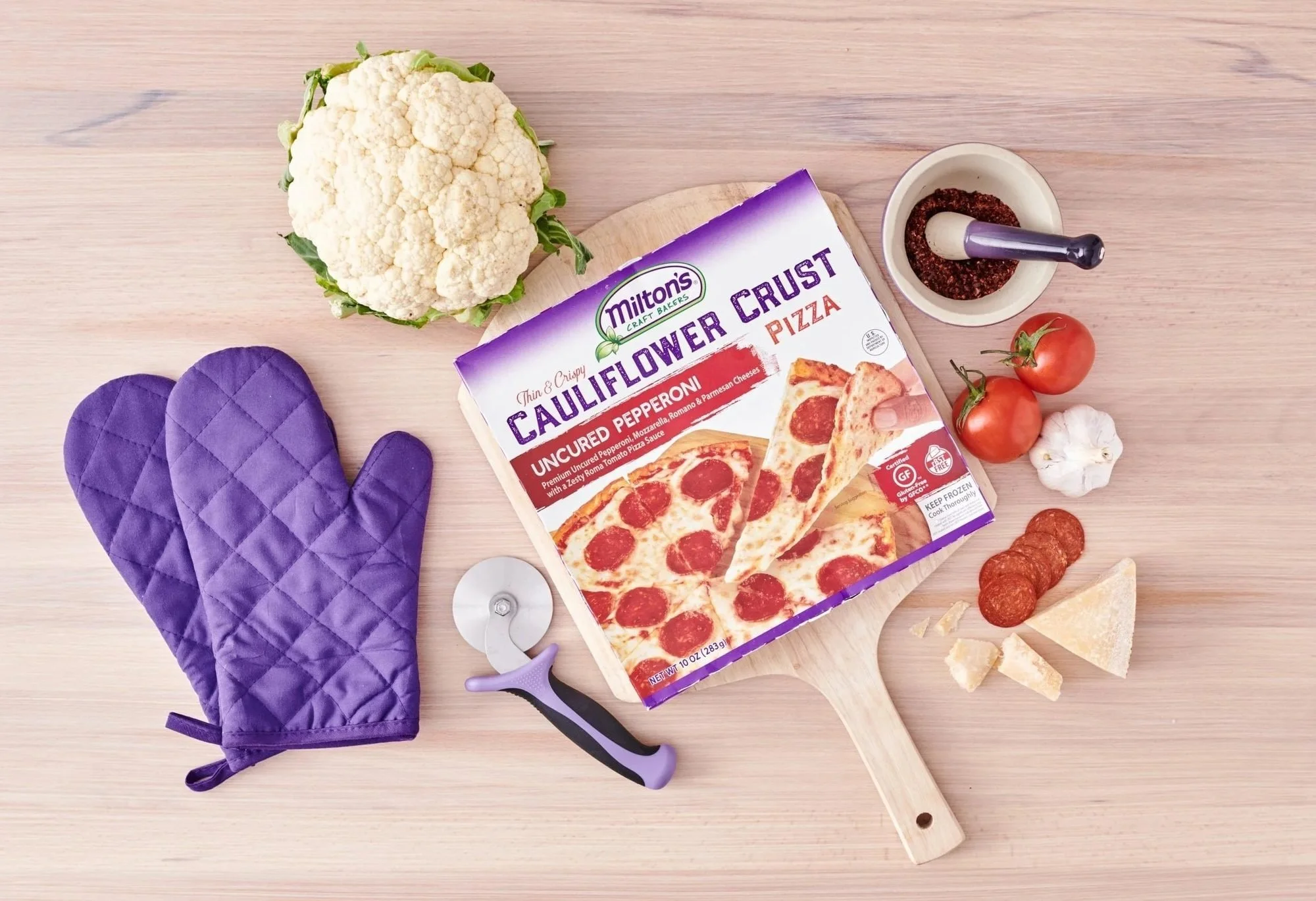 Cauliflower crust pizza box with oven mitts and toppings, frozen food CPG photography