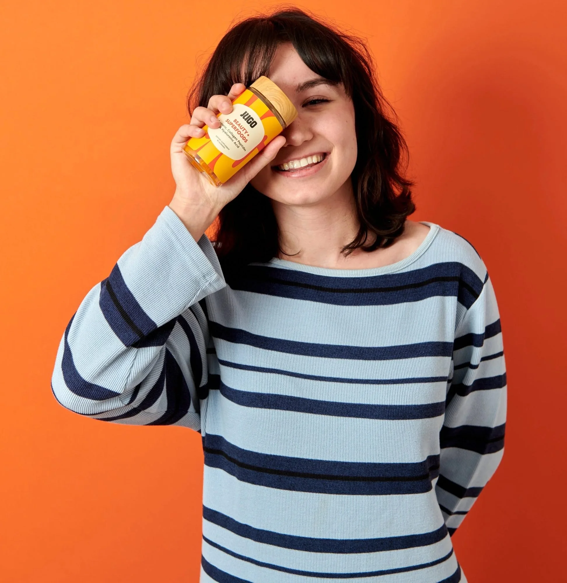 Smiling model holding a jar to her eye on orange, color-blocked CPG lifestyle photography