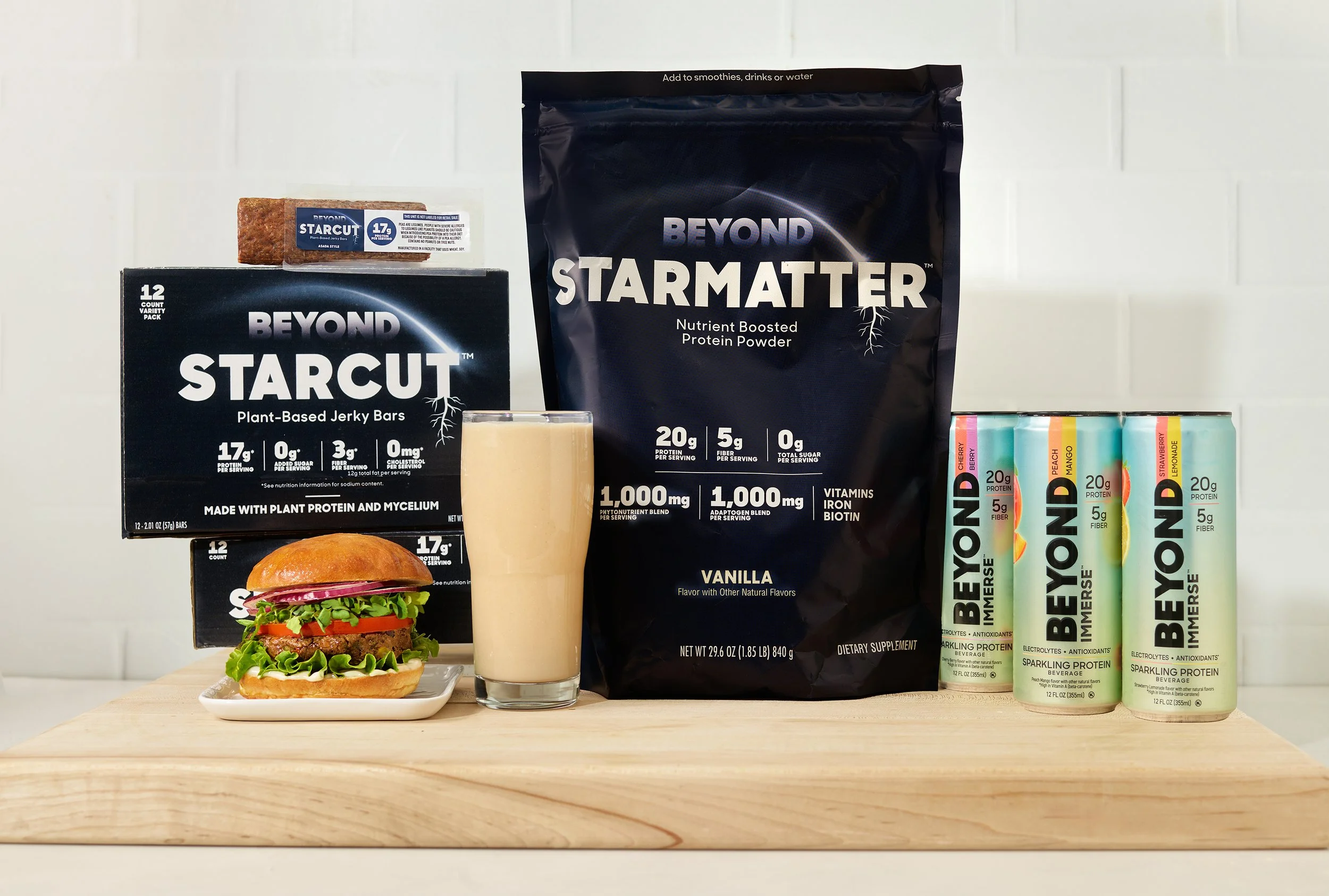 A plate with a plant-based burger containing lettuce, tomato, and a burger patty, placed on a wooden surface. Behind it are various health and protein products, including Beyond Meat plant-based jerky, Beyond StarMaker protein powder, and Beyond Mers