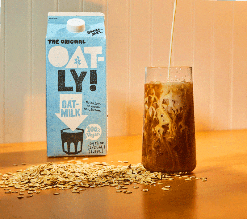 Oat milk poured into an iced chai next to an Oatly carton, beverage stop motion