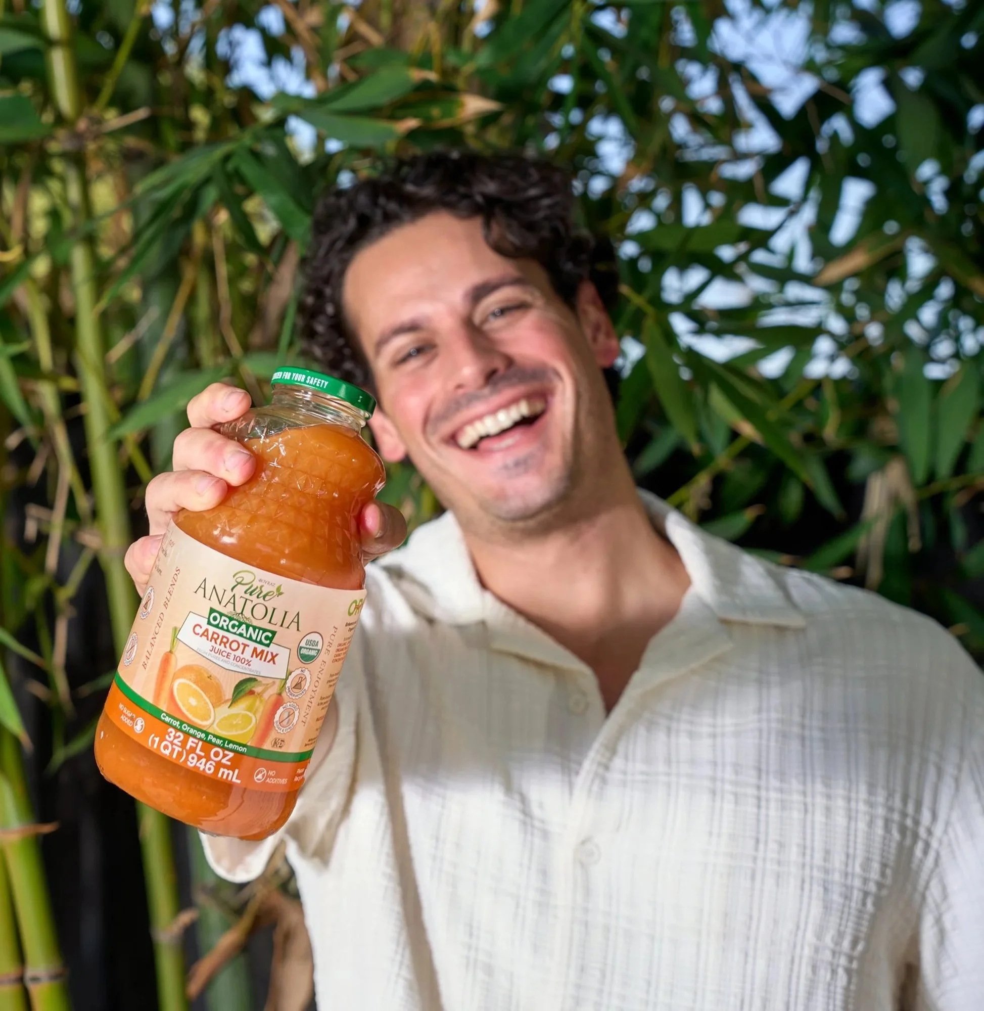 Laughing man holding a Pure Anatolia juice bottle in a bamboo garden, CPG lifestyle photography