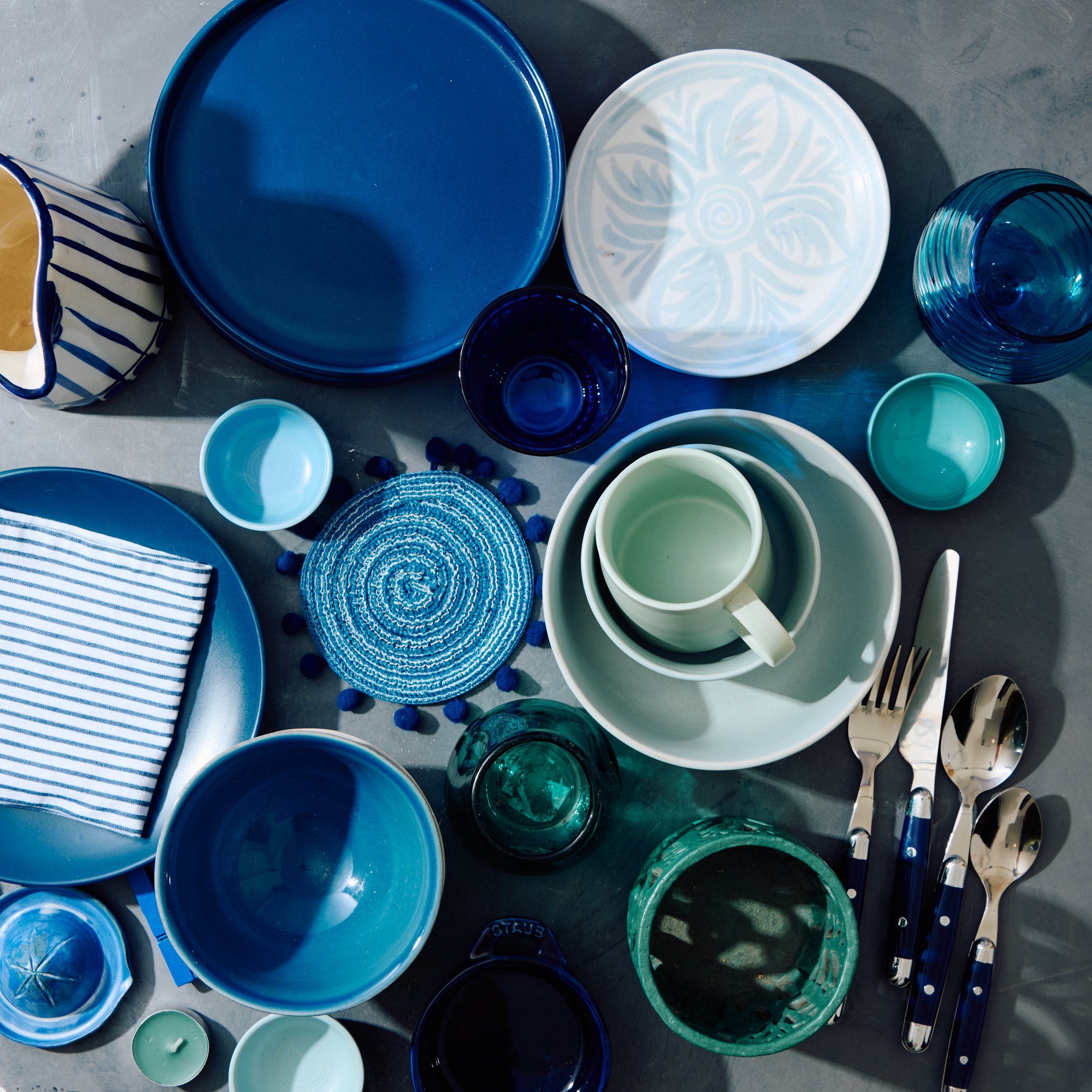 Arrangement of blue and white dishware including plates, bowls, glasses, cups, and cutlery on a table.