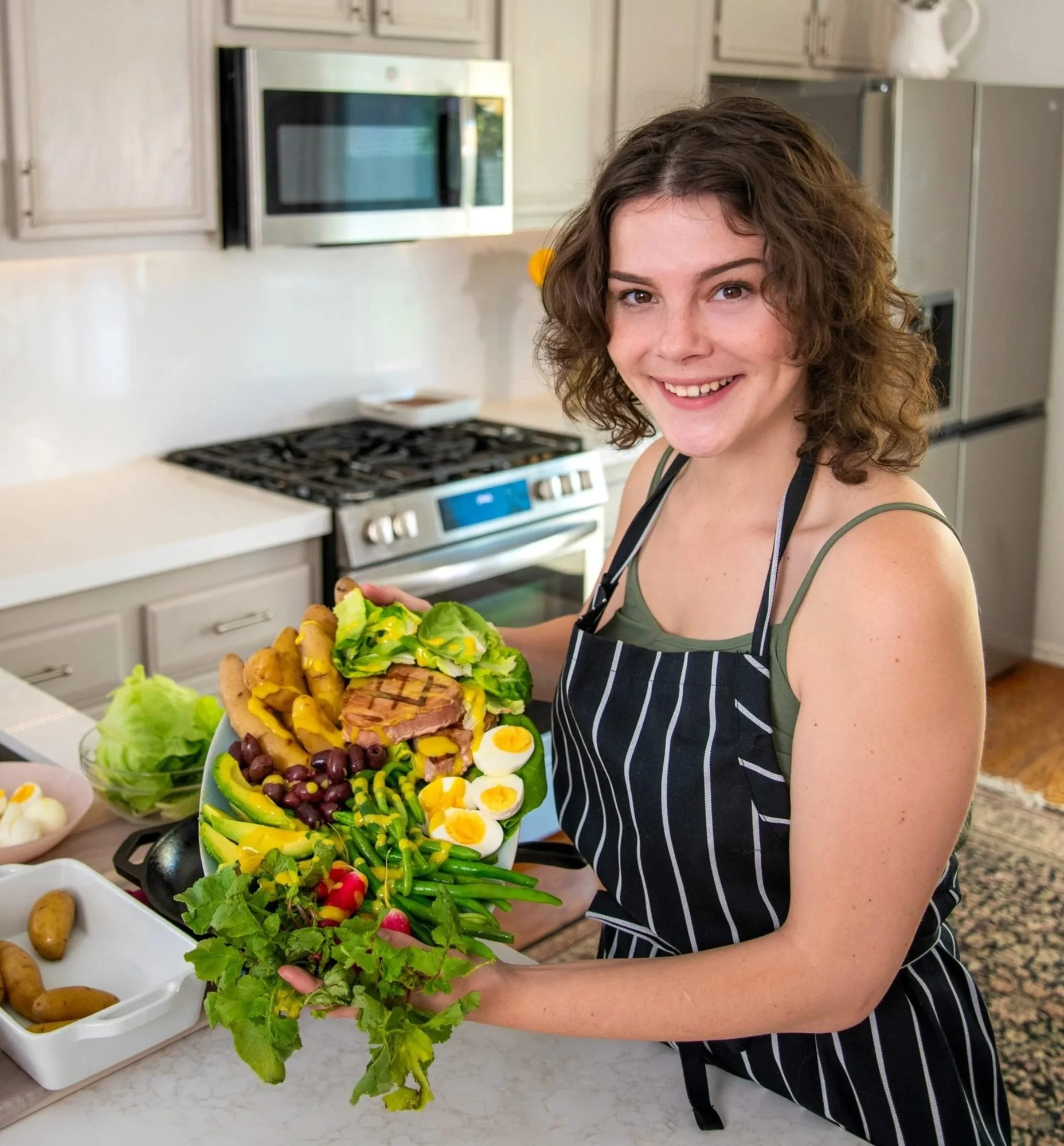 Woman in an apron serving a salad platter in a kitchen, food lifestyle photography